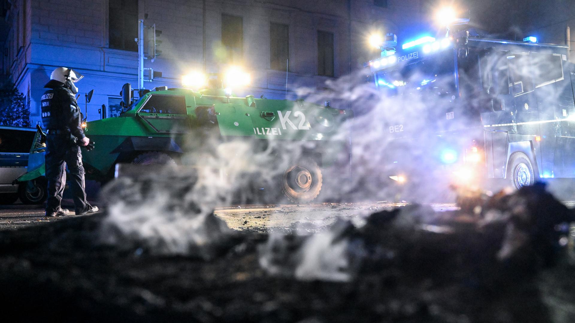Polizisten in Leipzig stehen hinter einer rauchenden Barrikade im Stadtteil Connewitz, die zuvor gelöscht wurde.