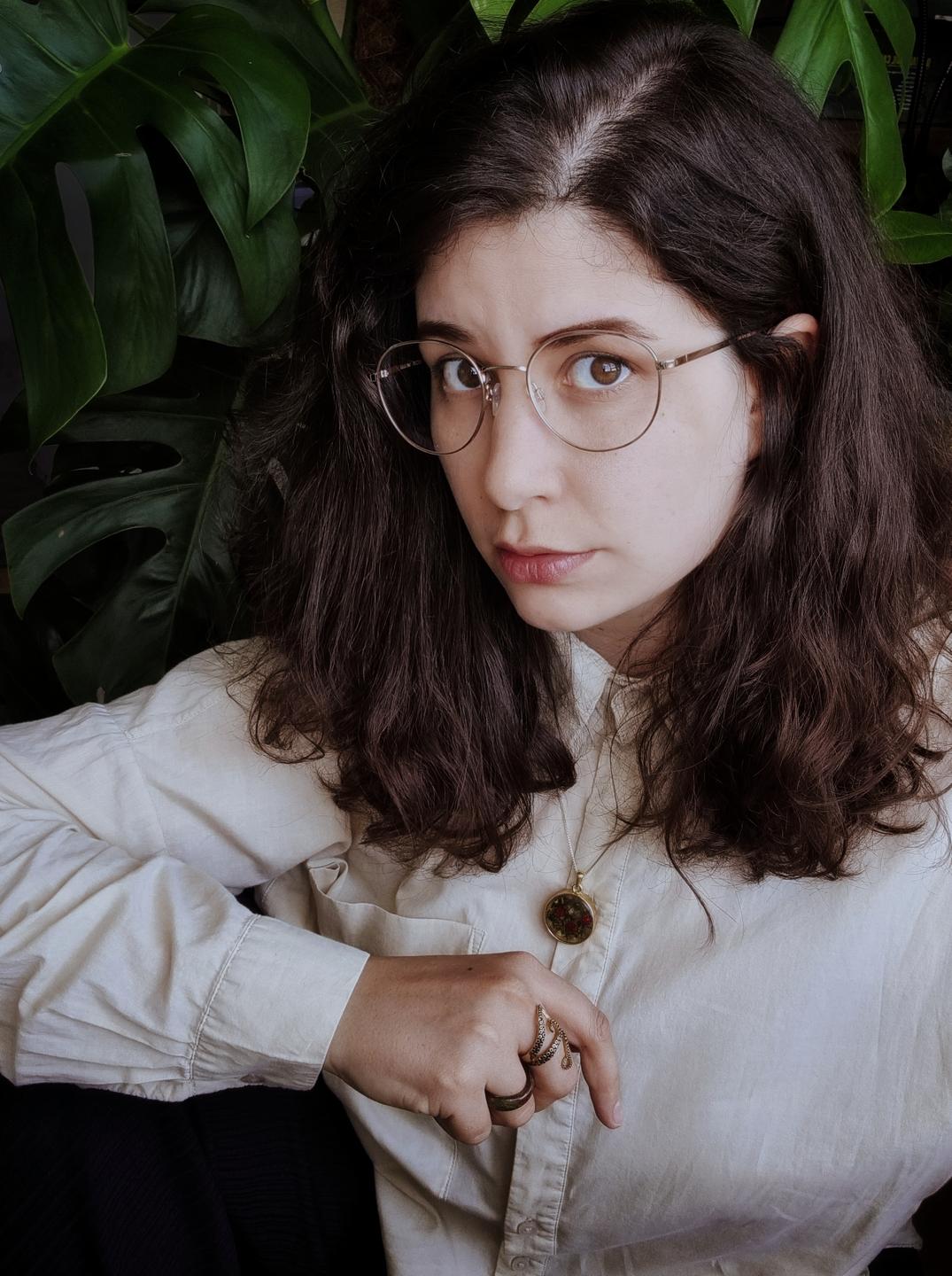 Selfie von Jasmin Schreiber mit großer Brille und offenen Haaren vor einem Hintergrund aus Blättern.