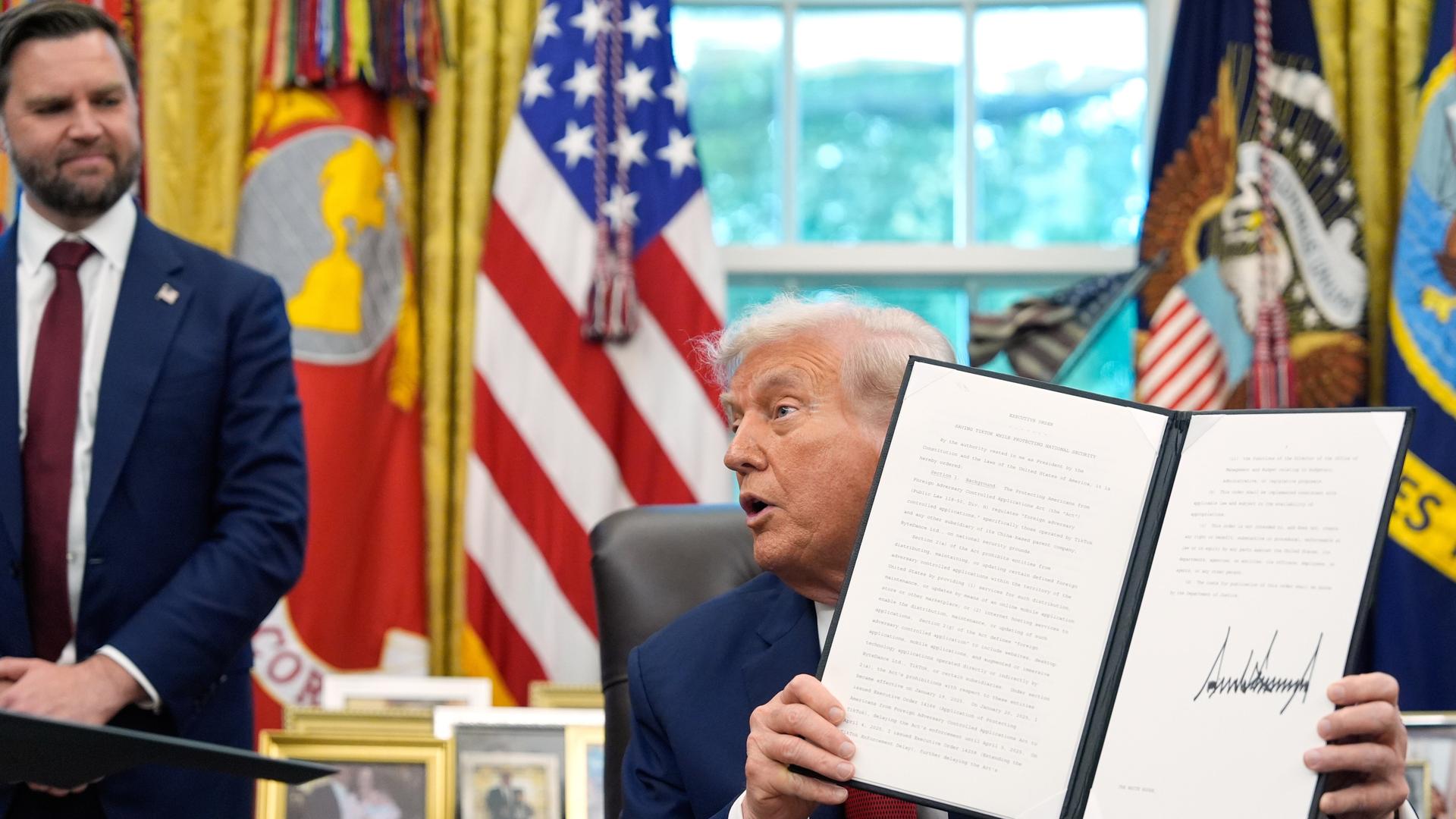 US-Präsident Donald Trump hält im Oval Office im Weißen Haus eine unterzeichnete Anordnung zu TikTok in der Hand. Vizepräsident JD Vance schaut im Hintergrund zu.