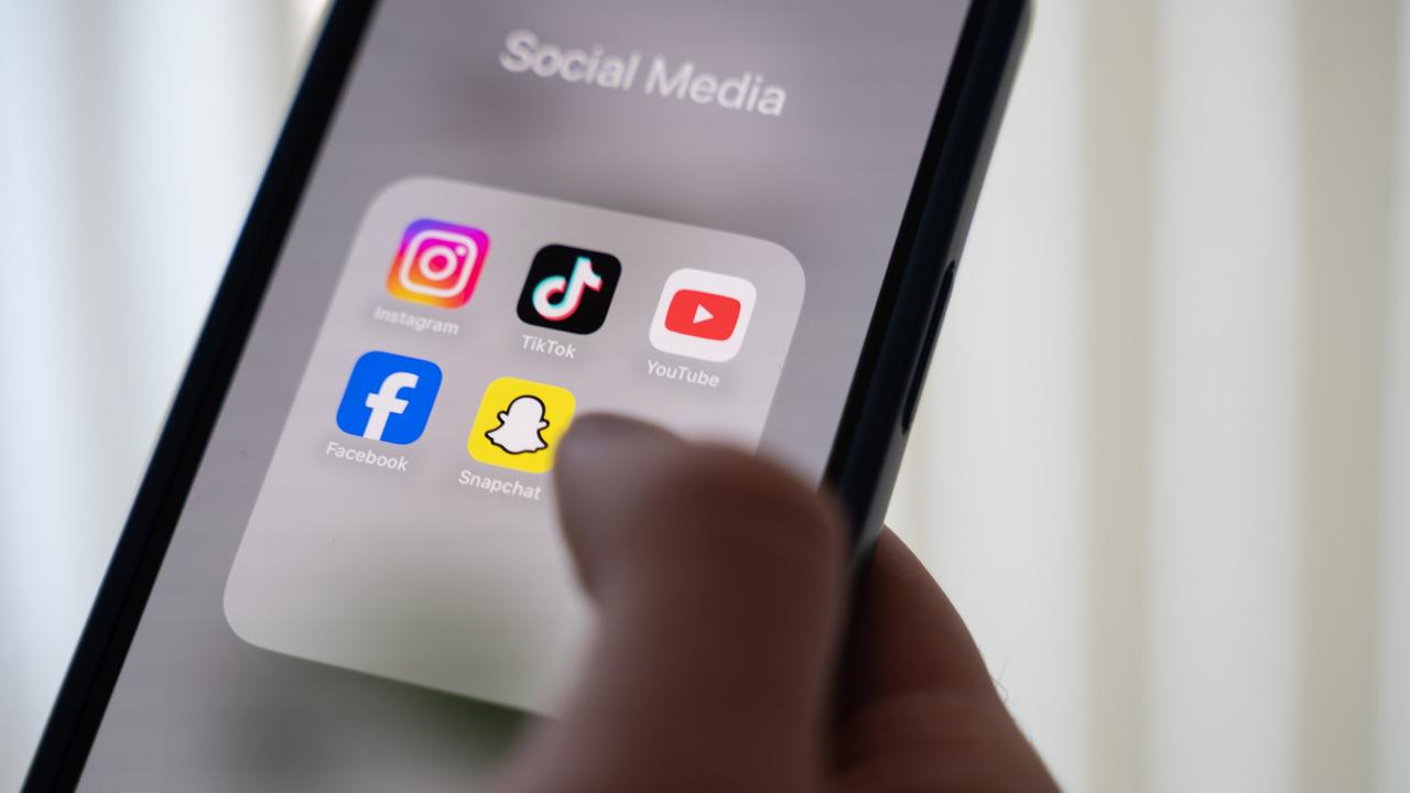 Eine junge Frau hält ein Smartphone, auf dessen Display verschiedene Social Media Apps angezeigt werden. 