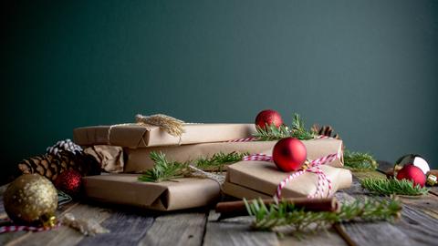 Ein Stapel weihnachtlich verpackter Geschenke auf einem Tisch zwischen Baumschmuck und Tannengrün
