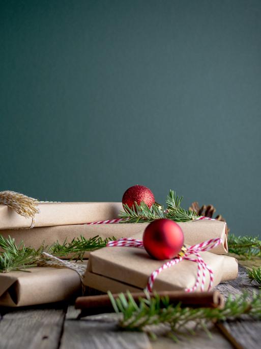 Ein Stapel weihnachtlich verpackter Geschenke auf einem Tisch zwischen Baumschmuck und Tannengrün