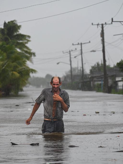 Ein Mann watet durch eine geflutete Straße, das Wasser reicht ihm bis zur Hüfte.