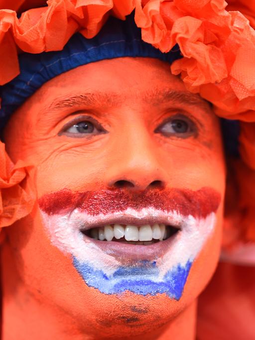 Ein Fan der niederländischen Fußballnationalmannschaft in einer Nahaufnahme. Das Gesicht des Mannes ist komplett orange bemalt, außerdem trägt er eine orangefarbene Perücke. 