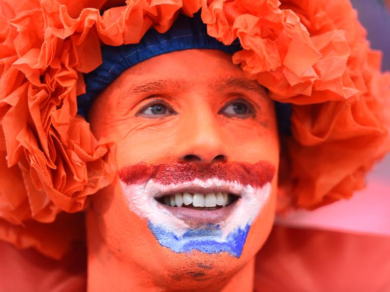 Ein Fan der niederländischen Fußballnationalmannschaft in einer Nahaufnahme. Das Gesicht des Mannes ist komplett orange bemalt, außerdem trägt er eine orangefarbene Perücke. 