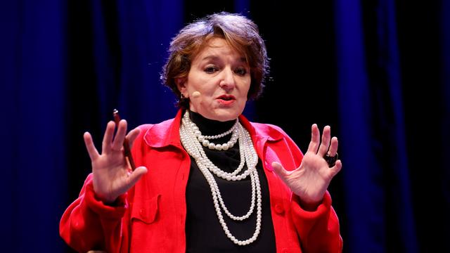 Die Soziologin Eva Illouz sitzt auf einer Podiumsbühne. Sie trägt eine rote Jacke, schwarzen Rollkragenpullover und mehrere helle Perlenketten um den Hals. Im Hintergrund: Ein dunkelblauer Vorhang.