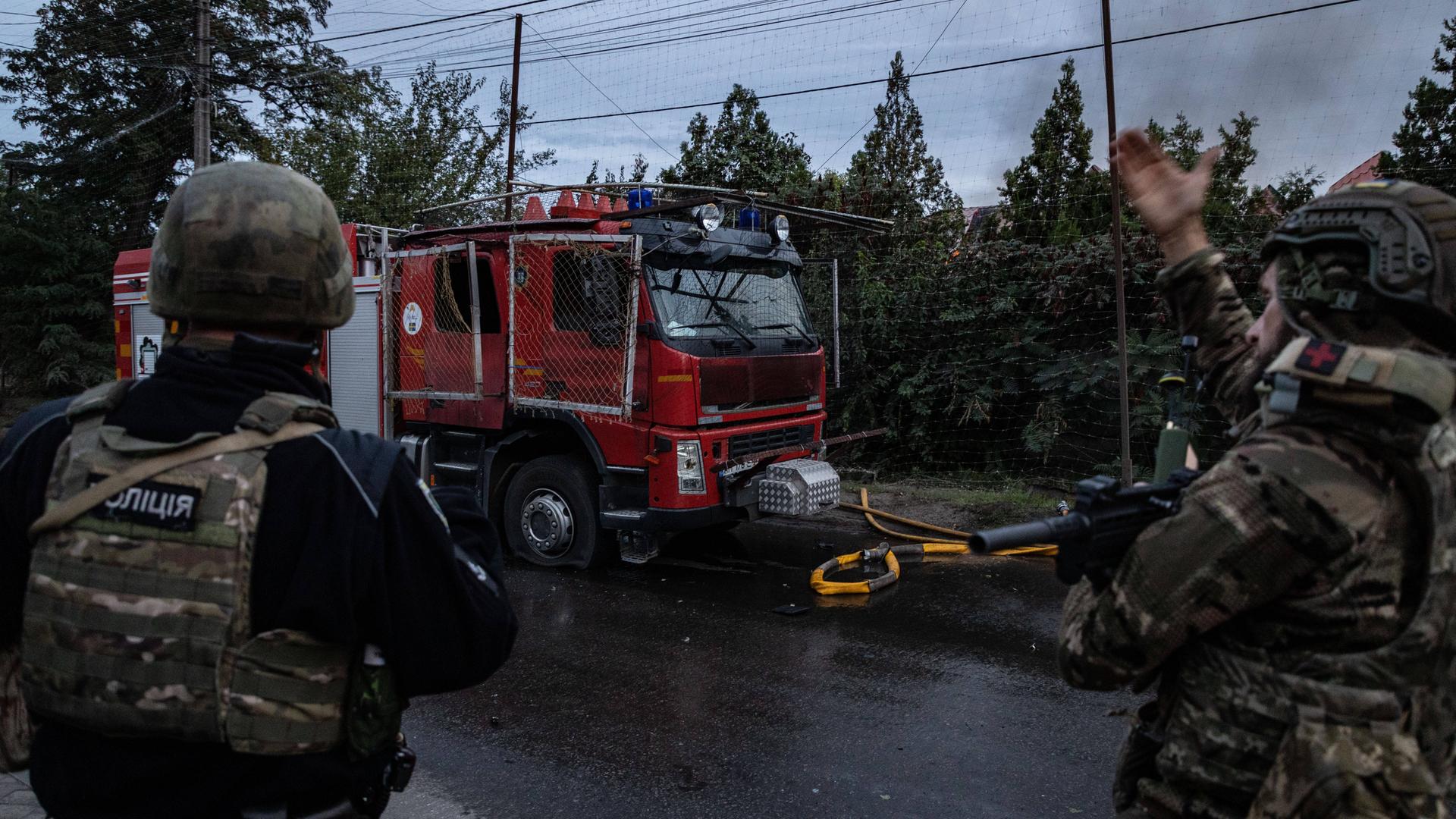 Angehörige der ukrainischen Streitkräfte regeln den Verkehr neben einem Feuerwehrwagen, nachdem dieser bei einem Hausbrand infolge eines russischen Drohnenangriffs von einer FPV-Drohne getroffen wurde. Angehörige der ukrainischen Streitkräfte regeln den Verkehr neben einem Feuerwehrwagen, nachdem dieser bei einem Hausbrand infolge eines russischen Drohnenangriffs von einer FPV-Drohne getroffen wurde.