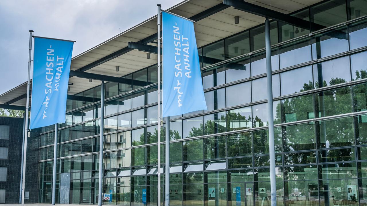 Vor der Glasfassade des MDR-Landesfunkhauses in Magdeburg sind zwei blaue Fahnen mit der weißen Aufschrift "mdr Sachsen-Anhalt" zu sehen.