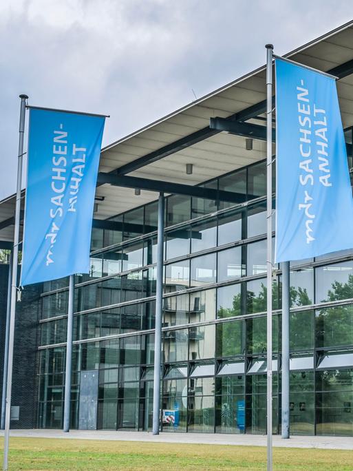 Vor der Glasfassade des MDR-Landesfunkhauses in Magdeburg sind zwei blaue Fahnen mit der weißen Aufschrift "mdr Sachsen-Anhalt" zu sehen.