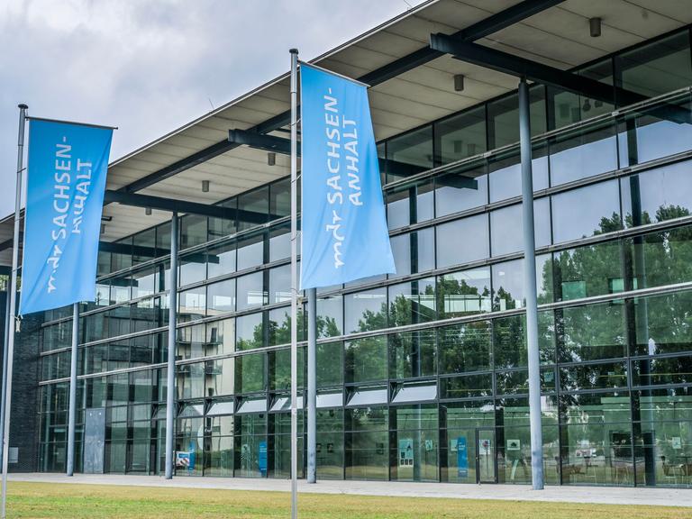 Vor der Glasfassade des MDR-Landesfunkhauses in Magdeburg sind zwei blaue Fahnen mit der weißen Aufschrift "mdr Sachsen-Anhalt" zu sehen.