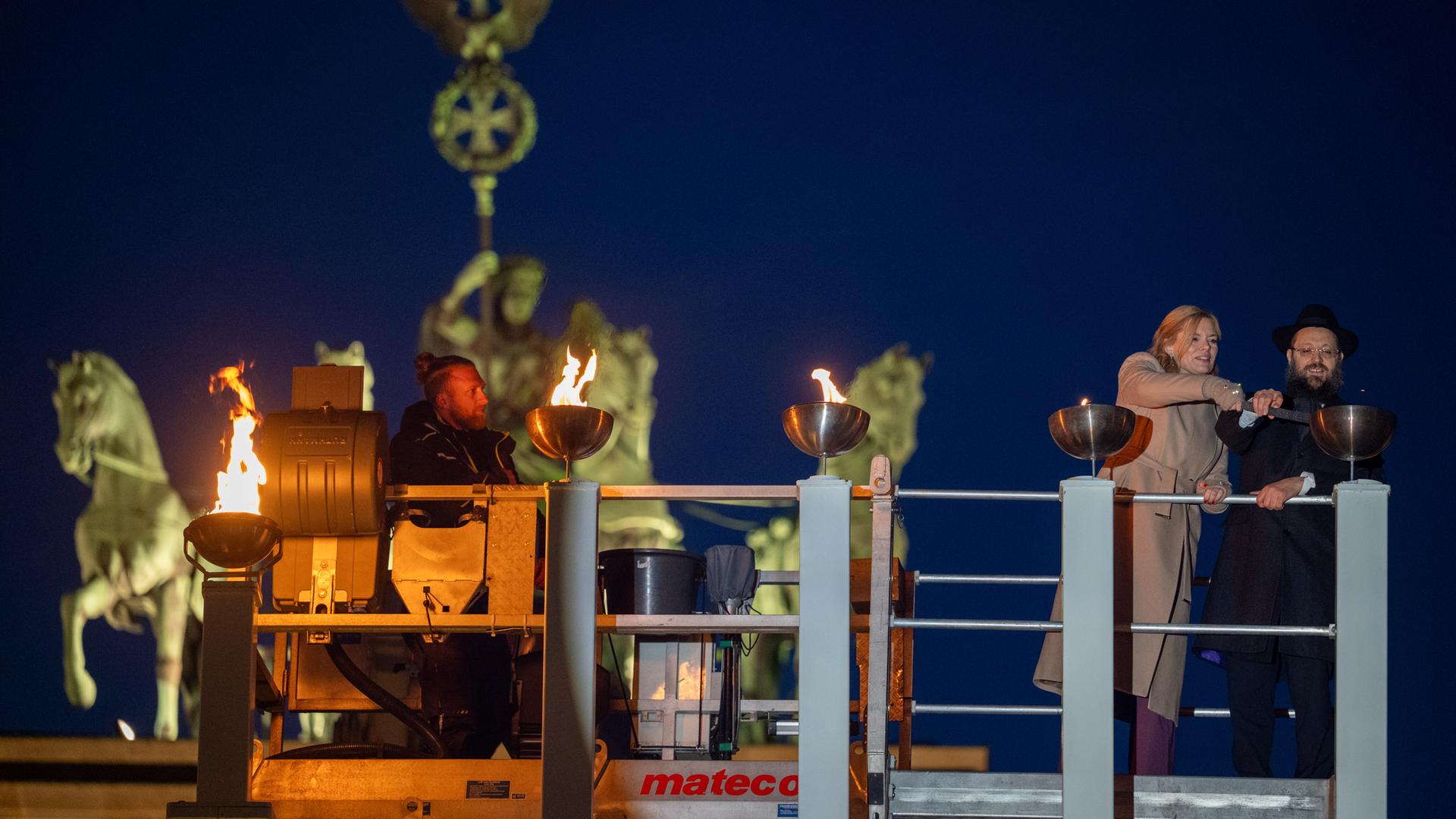 Bundestagspräsidentin Julia Klöckner (CDU) und Rabbiner Yehudi Teichtal entzünden am Brandenburger Tor während einer festlichen Zeremonie die Lichter am Chanukka-Leuchter mittels einer Fackel. Bundestagspräsidentin Julia Klöckner (CDU) und Rabbiner Yehudi Teichtal entzünden am Brandenburger Tor während einer festlichen Zeremonie die Lichter am Chanukka-Leuchter mittels einer Fackel.