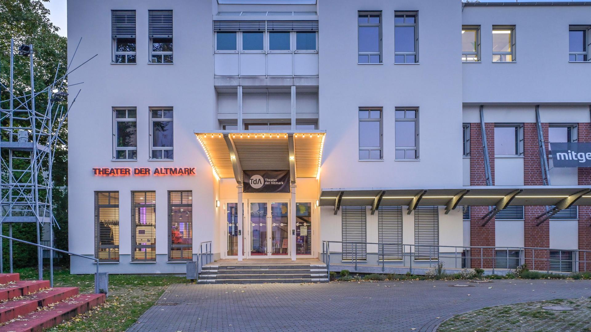 Theater der Altmark am frühen Abend. Das Gebäude ist zum Teil beleuchtet.