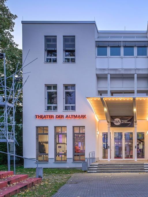 Theater der Altmark am frühen Abend. Das Gebäude ist zum Teil beleuchtet.
