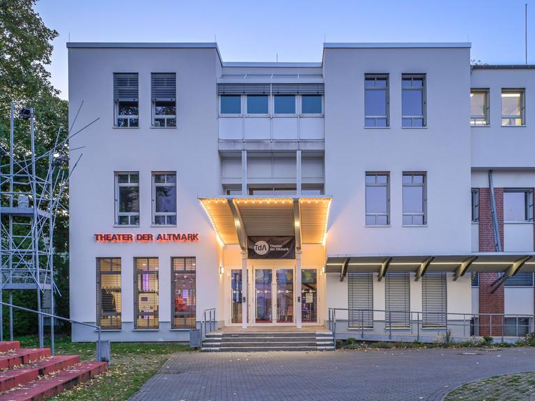 Theater der Altmark am frühen Abend. Das Gebäude ist zum Teil beleuchtet.