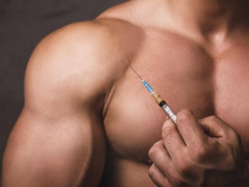 Ein muskulöser Mann hält eine Spritze mit anabolen Steroiden in die Kamera (Symbolbild).