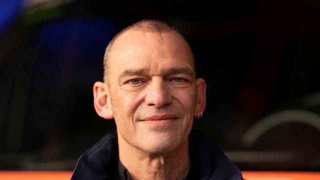 Albi Roebke trägt eine Jacke der Notfallseelsorge und steht vor einem Rettungswagen.