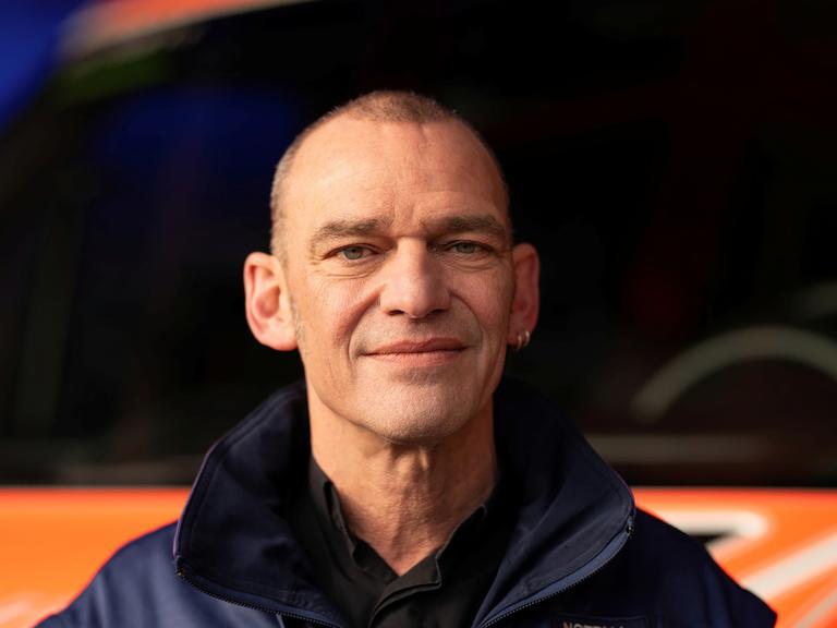 Albi Roebke trägt eine Jacke der Notfallseelsorge und steht vor einem Rettungswagen.