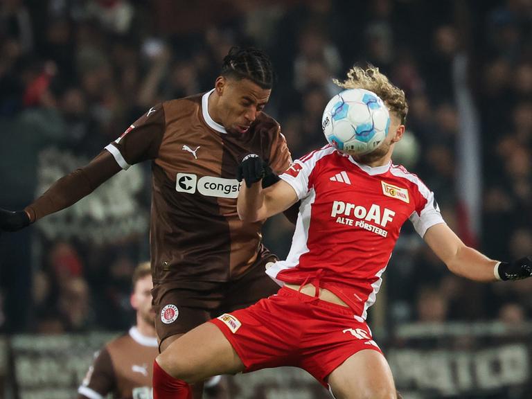 Die beiden springen zum Kopfball hoch. Guliavogui trägt ein braunes Trikot; Hollerbach ein weiß-rotes. Sein Kopf ist vom Ball verdeckt. 