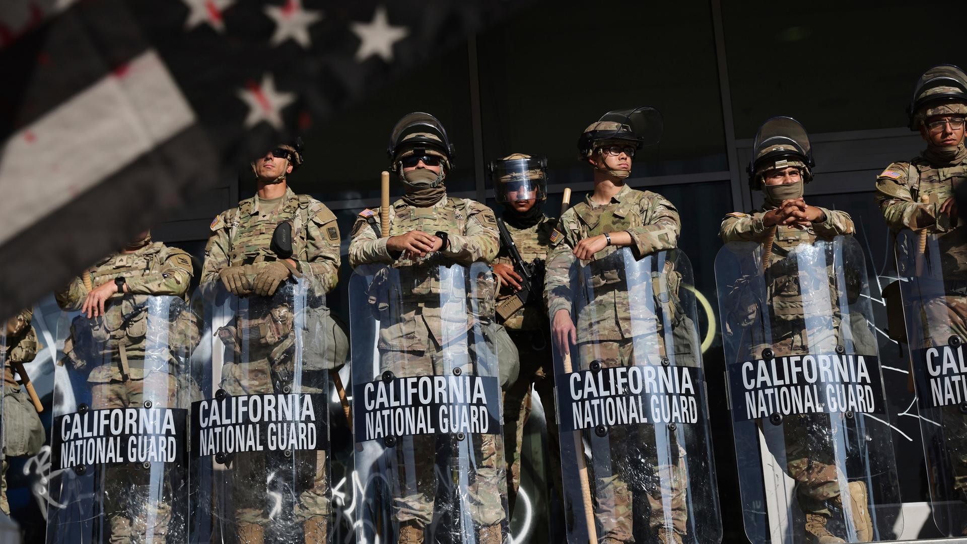 Soldaten der Nationalgarde sind während Protesten als Reaktion auf eine Reihe von Razzien der Einwanderungs- und Zollbehörde der Vereinigten Staaten (ICE) im ganzen Land in der Nähe eines Eingangs zu einem Bundesgebäude in Los Angeles postiert. Soldaten der Nationalgarde sind während Protesten als Reaktion auf eine Reihe von Razzien der Einwanderungs- und Zollbehörde der Vereinigten Staaten (ICE) im ganzen Land in der Nähe eines Eingangs zu einem Bundesgebäude in Los Angeles postiert.