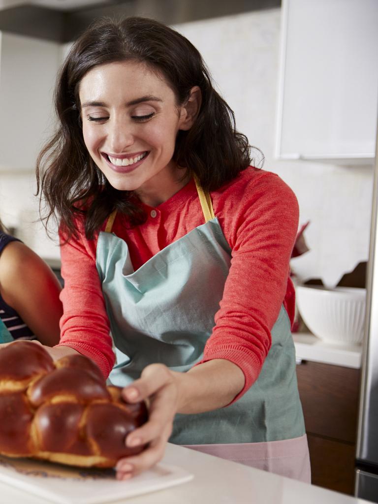 Eine Frau mit braunen Haaren und mit Schürze steht in der Küche. Sie hält einen Hefezopf in der Hand. Links neben hier steht ihre Tochter. Eine Frau mit braunen Haaren und mit Schürze steht in der Küche. Sie hält einen Hefezopf in der Hand. Links neben hier steht ihre Tochter.