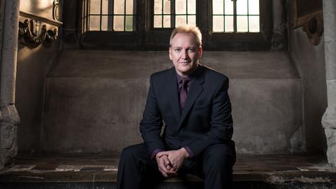 Nigel Short sitzt in einer Kirchennische und lächelt in die Kamera.