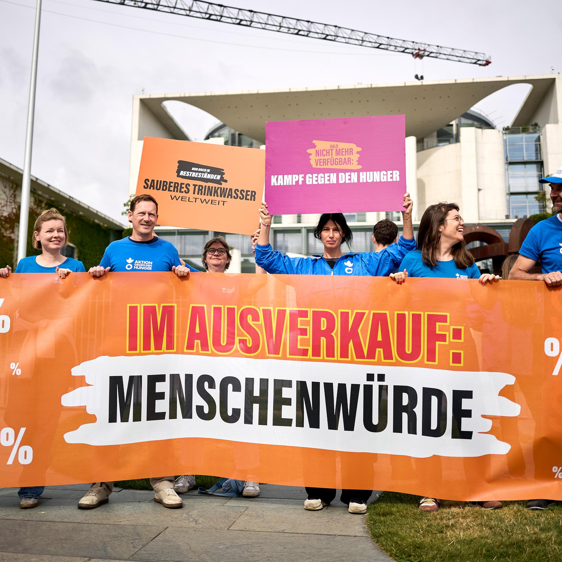 Demonstrierende stehen mit Transparenten, unter anderem mit dem Aufdruck "Im Ausverkauf: Menschenwürde", und Schildern vor dem Bundeskanzleramt.