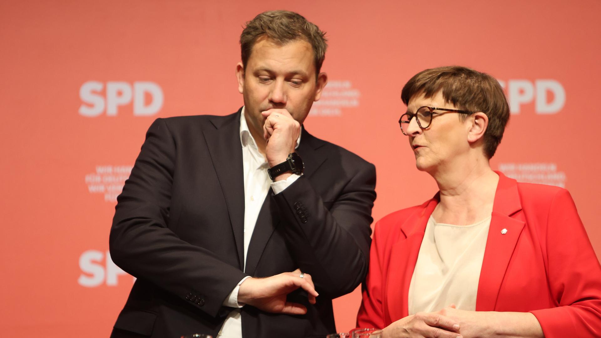 Lars Klingbeil und Saskia Esken stehen nebeneinander vor einer roten Wand auf einer Bühne. Klingbeil (li) trägt ein braunes Jacket, Esken (re) ein rotes Jacket, sie haben beide kurze braune Haare. Lars Klingbeil und Saskia Esken stehen nebeneinander vor einer roten Wand auf einer Bühne. Klingbeil (li) trägt ein braunes Jacket, Esken (re) ein rotes Jacket, sie haben beide kurze braune Haare.