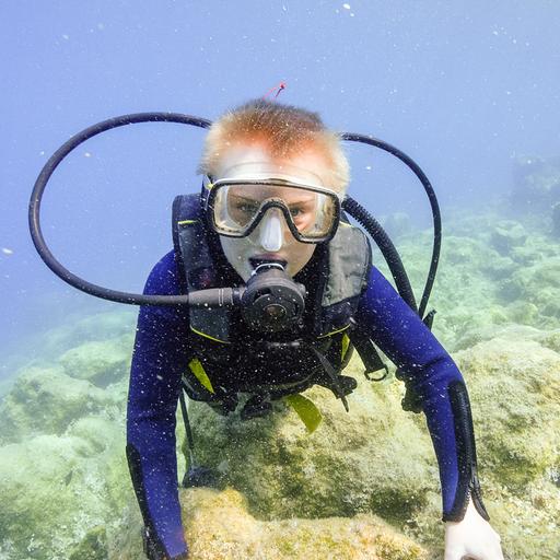 Ein Junge in voeller tauchermontur unter Wasser schaut in die Kamera