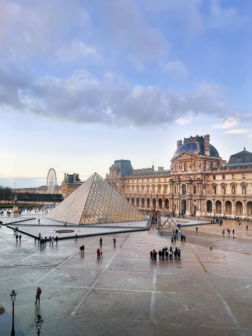Außenaufnehme des Louvre in Paris vor wolkigem Himmel.