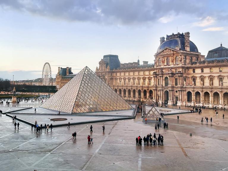 Außenaufnehme des Louvre in Paris vor wolkigem Himmel.