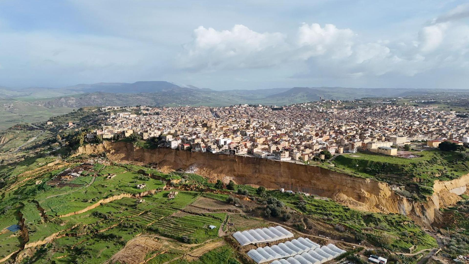 Eine Luftaufnahme zeigt die sehr lange Abbruchkante in der Stadt Niscemi. Von dort aus geht es einige Meter hinunter bis zum nächsten Plateau. Direkt am Abhang stehen einige Häuser.