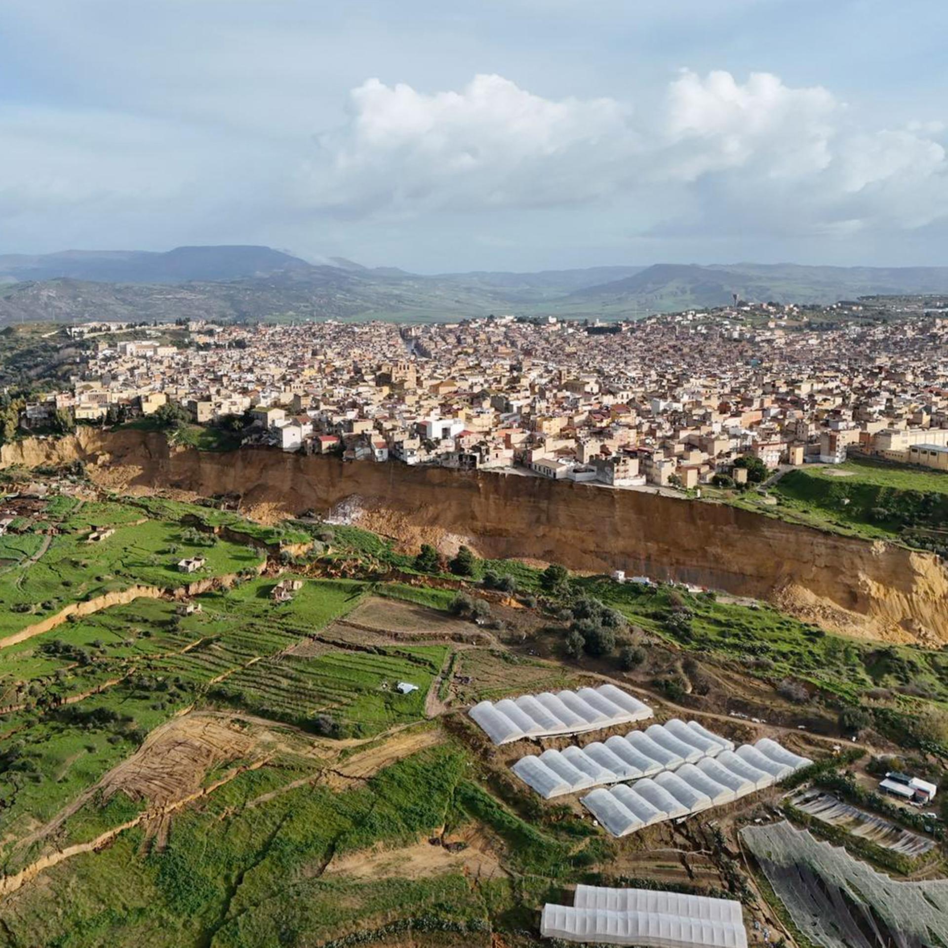 Eine Luftaufnahme zeigt die sehr lange Abbruchkante in der Stadt Niscemi. Von dort aus geht es einige Meter hinunter bis zum nächsten Plateau. Direkt am Abhang stehen einige Häuser.