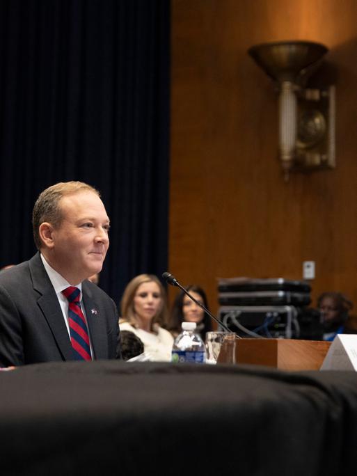 Der US-Rebublikaner Lee Zeldin sitzt an einem Pult. Hinter ihm sind mehrere Personen. 