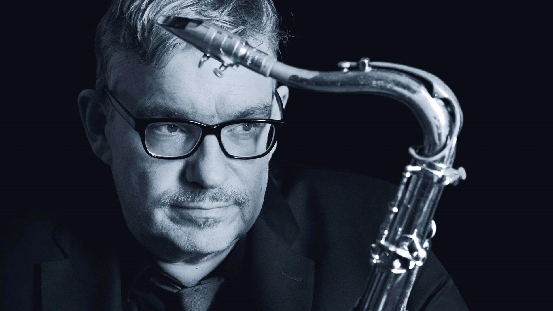 Ein Mann mit Brille und kurzem Haar umarmt sein Saxophon.