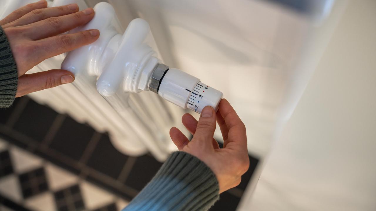 Eine Frau regelt in der kalten Jahreszeit zu Hause die Heizung am Thermostat.