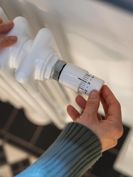 Eine Frau regelt zu Hause die Heizung am Thermostat.