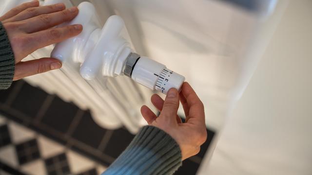 Eine Frau regelt in der kalten Jahreszeit zu Hause die Heizung am Thermostat.