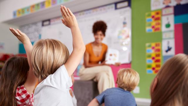 Eine Erzieherin sitzt vor einer Kinder-Gruppe in der Kita.