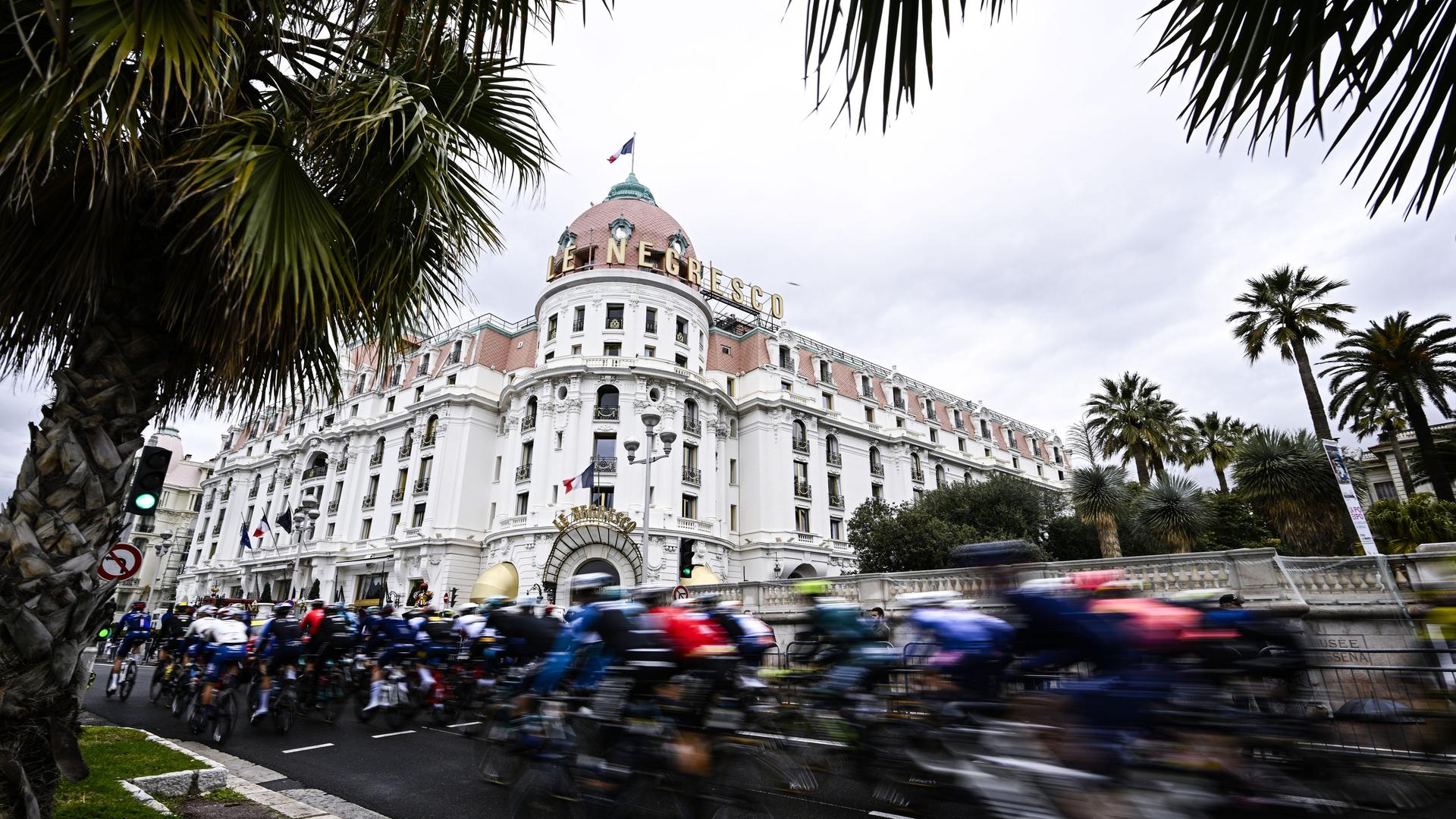 Das Foto zeigt den Start der siebten Etappe des achttägigen Radrennens Paris-Nizza an der Uferpromenade Promenade des Anglais in Nizza. Radfahrer sind verschwommen zu sehen. Im Hintergrund steht das bekannte Hotel Negresco.  