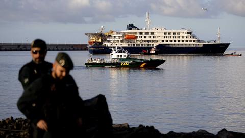 Das Kreuzfahrtschiff "Hondius" liegt im Wasser vor einer Küste, daneben ist ein Schiff der Küstenwache.