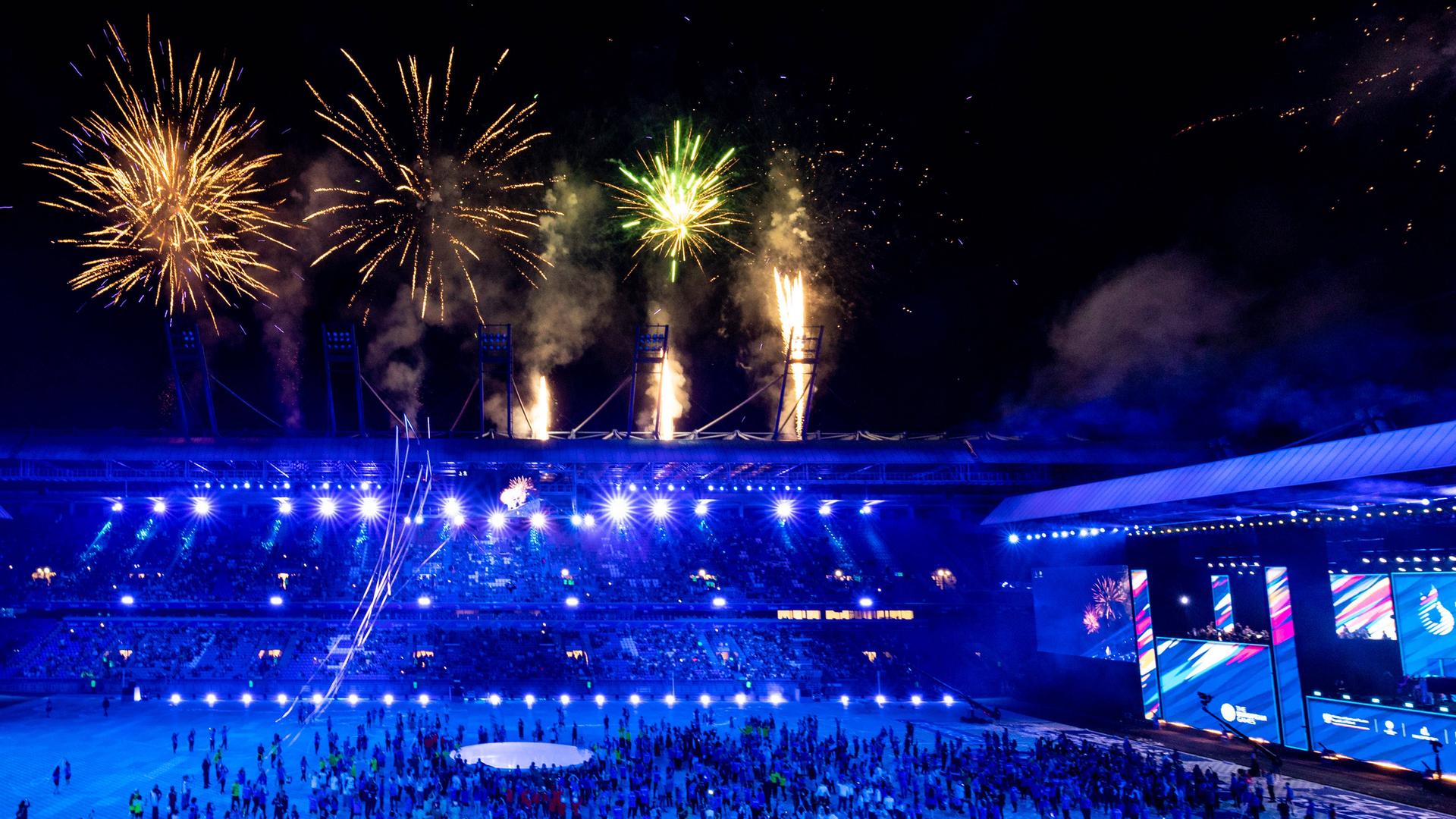 Feuerwerk über einem Stadion, das mit dunkelblauem Licht geflutet wird.