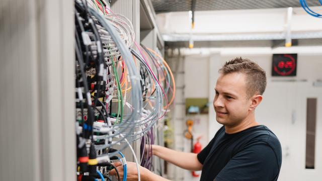 Ein junger Mann arbeitet in einem Geräteraum an einem Server mit vielen bunten Kabeln