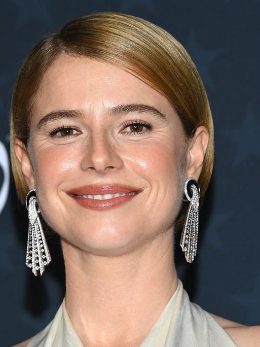 Eine Frau mit langen silbernen Ohrringen lächelt in die Kamera.