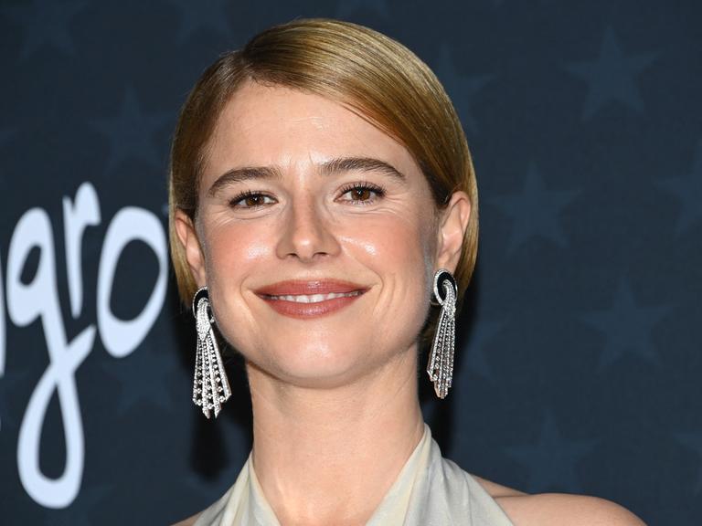 Eine Frau mit langen silbernen Ohrringen lächelt in die Kamera.