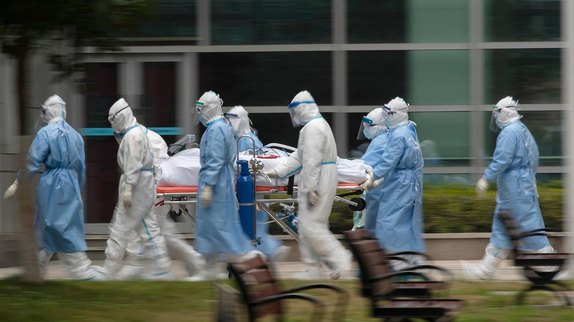 Menschen in Schutzkleidung transportieren einen Patienten. 