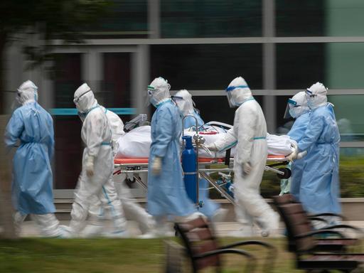 Menschen in Schutzkleidung transportieren einen Patienten. 