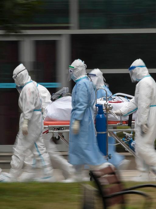 Menschen in Schutzkleidung transportieren einen Patienten. 