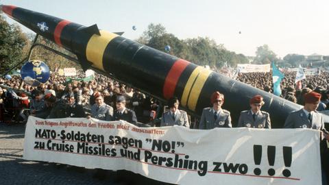 Soldaten der Bundeswehr in Uniform laufen mit einem Transparent und einer Pershing-II-Attrappe bei einer Demonstration gegen die NATO-Hochrüstung.