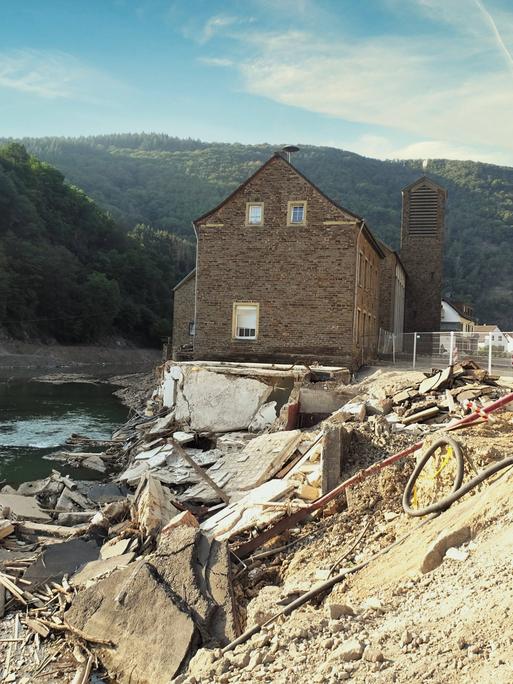 Ein Haus steht inmitten zerstörter Fundamente direkt am Fluss.