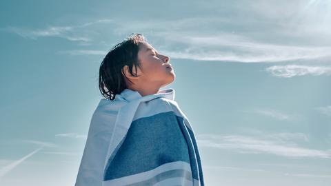Ein Junge, eingewickelt in eine Decke, steht mit geschlossenen Augen vor blauem Himmel und atmet bewusst ein und aus. Ein Junge, eingewickelt in eine Decke, steht mit geschlossenen Augen vor blauem Himmel und atmet bewusst ein und aus.